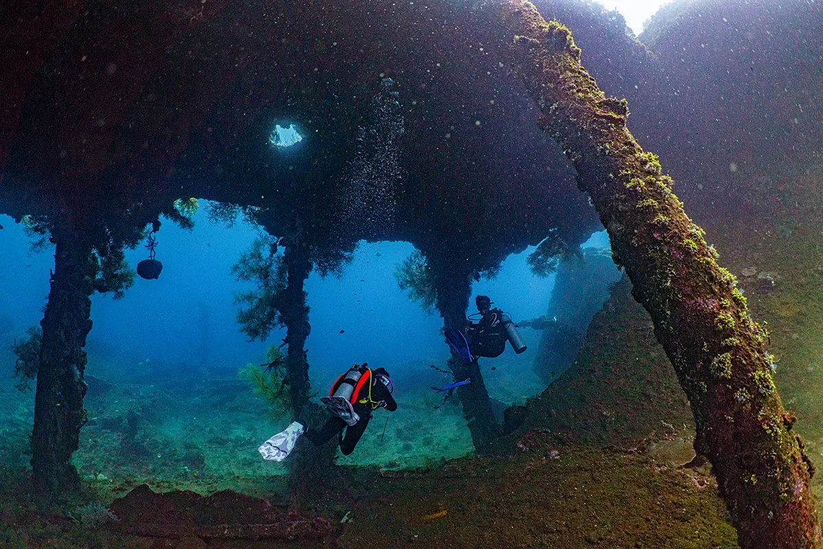 Divers swimming through the structure of the USAT Liberty Wreck in Tulamben